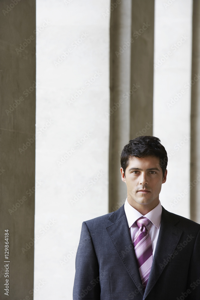 Portrait of serious young man in business suit standing by pillar
