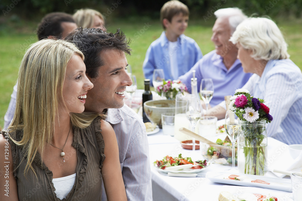 Happy loving couple at dining table with family in background