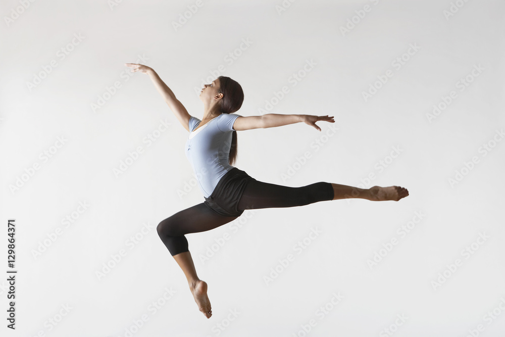 Fototapeta Full length of female ballet dancer leaping in mid air isolated on white background