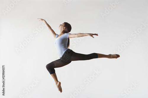 Full length of female ballet dancer leaping in mid air isolated on white background