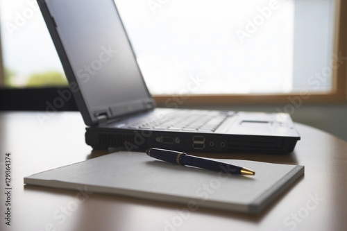Notepad with pen and laptop on desk