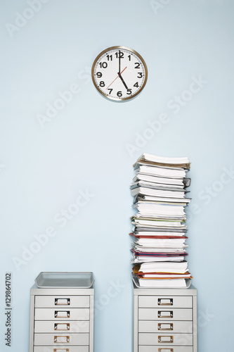 Office wall with clock stack of paperwork in outbox on file cabinet
