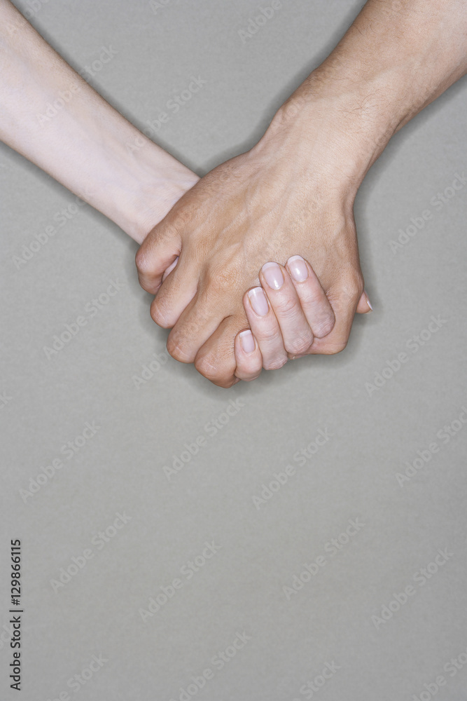 Closeup of couple holding hands against gray background Closeup of couple holding hands against gray background