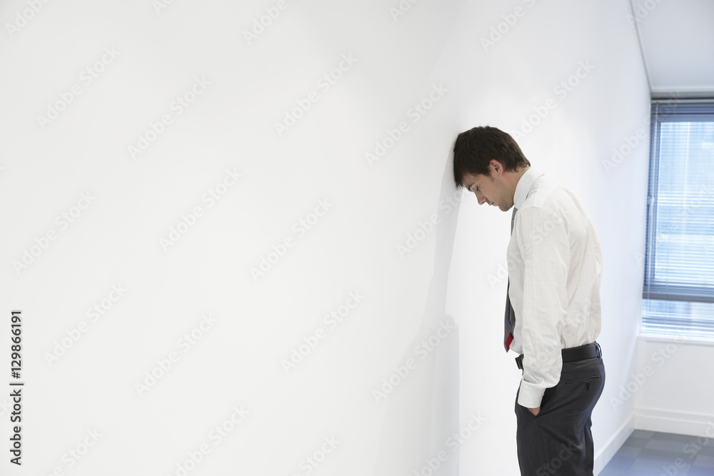 Side view of an unhappy businessman resting head against office wall 