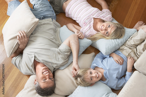Portrait of happy family of three lying on floor with cushions at home