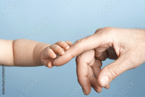 Closeup of a baby holding man's finger against blue background photo