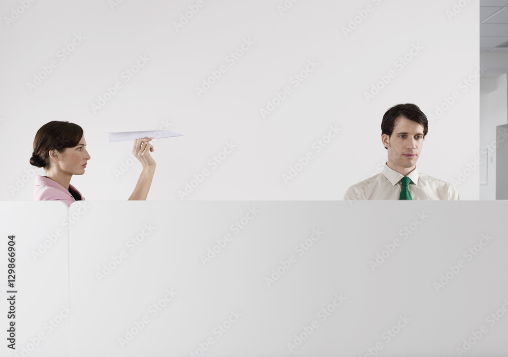 Female executive throwing a paper aeroplane at male colleague in the office Female executive throwing a paper aeroplane at male colleague in the office