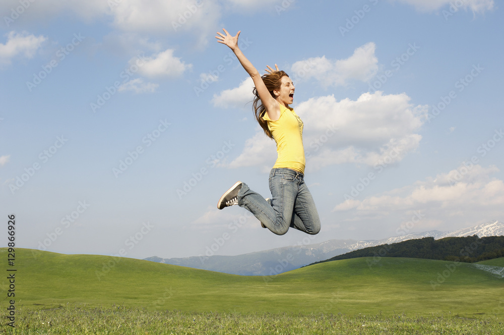 Side view of young woman with arms raised screaming while jumping in park Side view of young woman with arms raised screaming while jumping in park