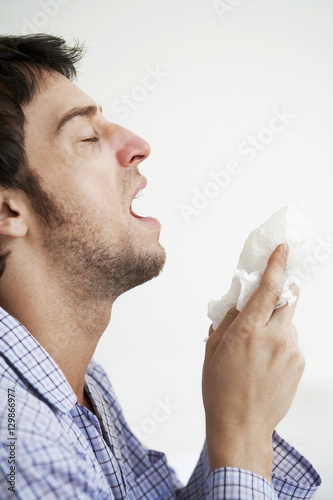 Young man holding tissue paper about to sneeze over white background