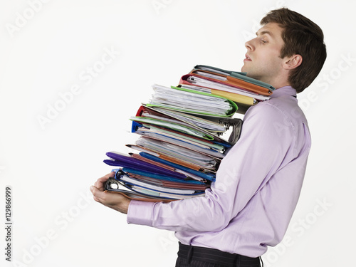 Male office worker carrying heavy binders against white background