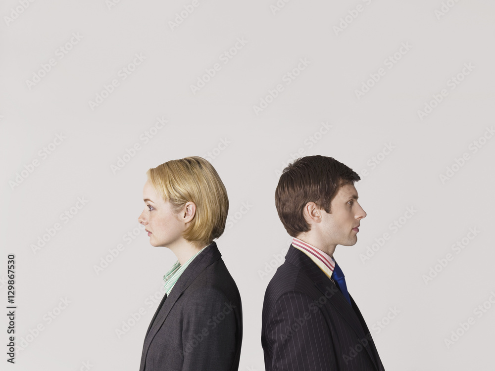 Side view of two business people standing back to back on gray background Side view of two business people standing back to back on gray background