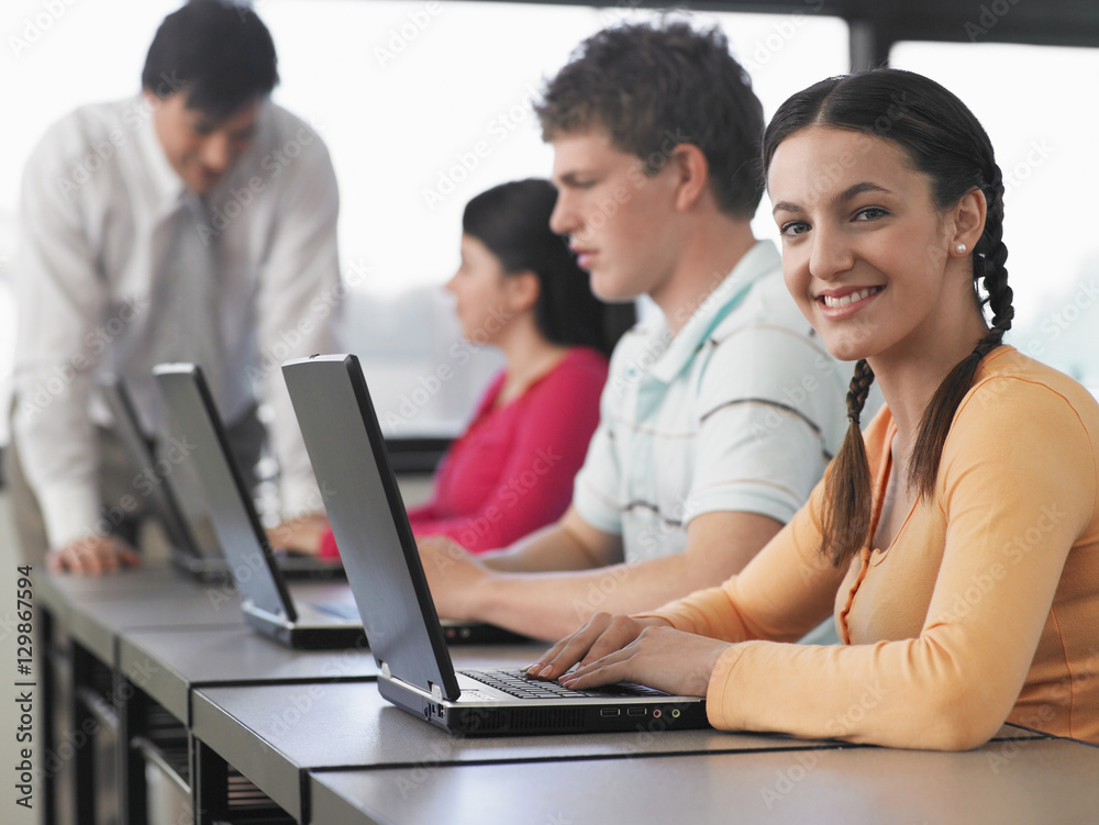 Portrait of teenage girl with classmates using laptops in computer class