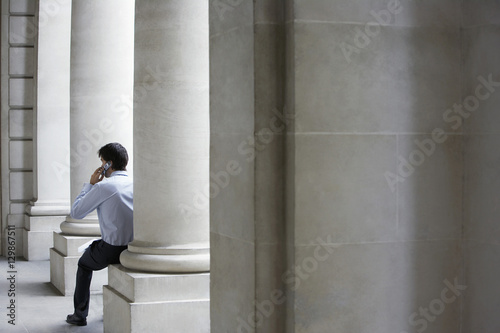 Rear view of businessman using mobile phone while sitting against building pillar