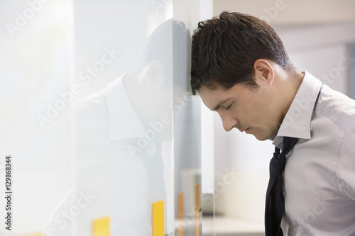 Canvas Print Side view of an unhappy businessman resting head against office wall
