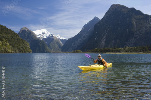 Young man kayaking in peaceful lake with mountains in background