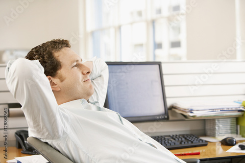 Obraz na plátně Young businessman reclining in office chair at desk