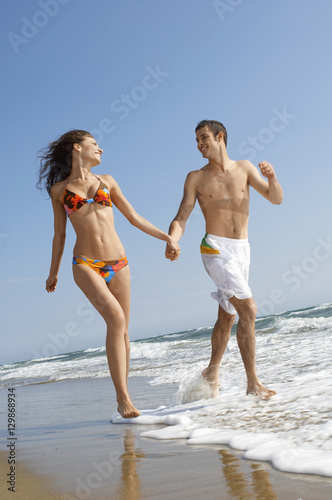 Young loving couple holding hands while running in surf at beach