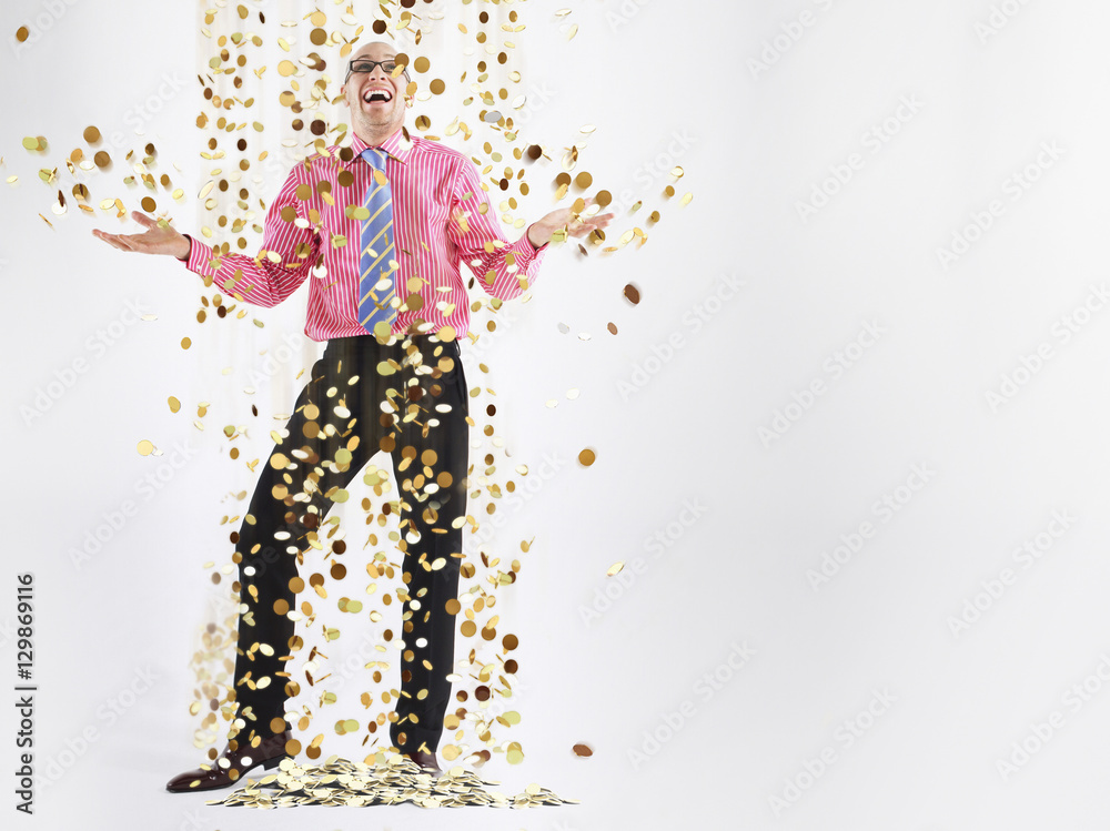 Obraz premium Full length of a happy male executive under shower of gold coins against white background