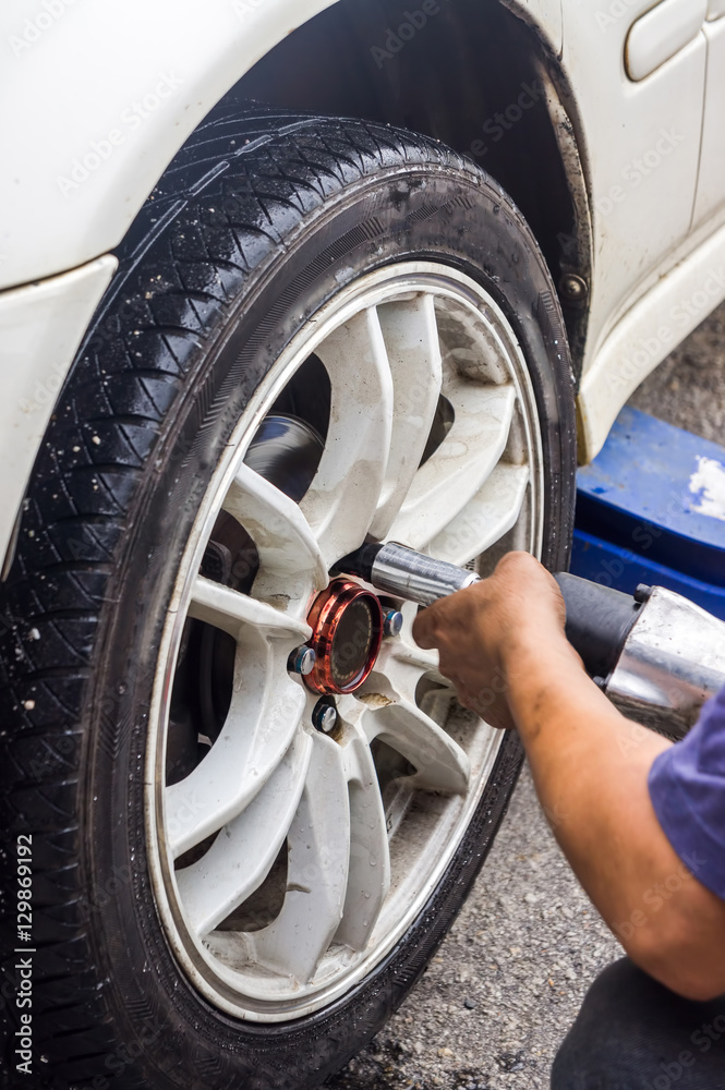 Detail image of mechanic hands with tool, changing tyre of car, with blurred background of garage. Soft focus with motion on hand. Detail image of mechanic hands with tool, changing tyre of car, with blurred background of garage. Soft focus with motion on hand.