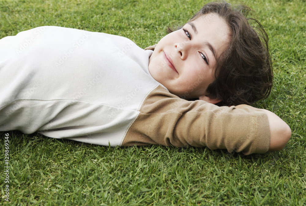 Side view portrait of cute elementary boy with hands behind head lying on grass Side view portrait of cute elementary boy with hands behind head lying on grass