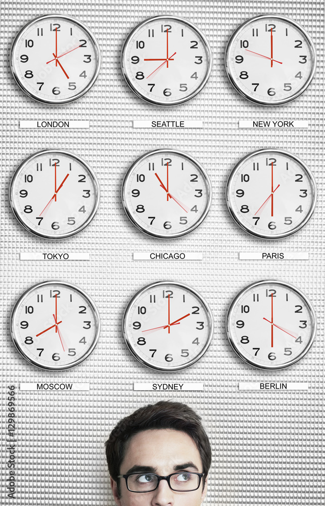 Fototapeta premium Young businessman in front of clocks showing time across the world