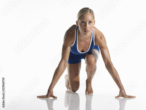 Portrait of a young female athlete in starting position against white background