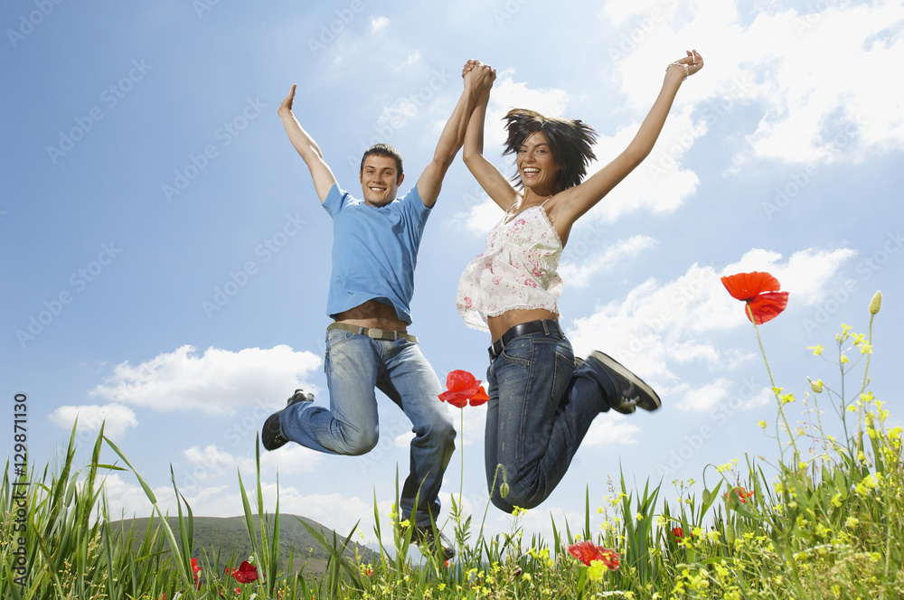 Low angle portrait of young multiethnic couple jumping in poppy field against sky Low angle portrait of young multiethnic couple jumping in poppy field against sky