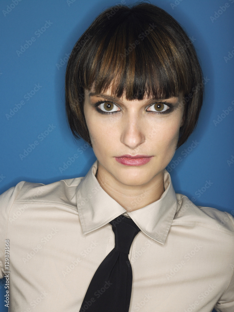 Closeup portrait of a bobbed haired young woman wearing tie against blue background Closeup portrait of a bobbed haired young woman wearing tie against blue background