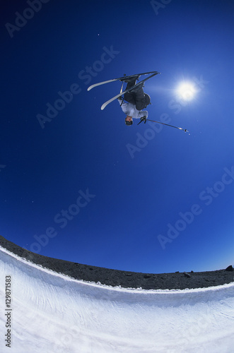 Skier performing flip on mountain against clear blue sky with fisheye shot
