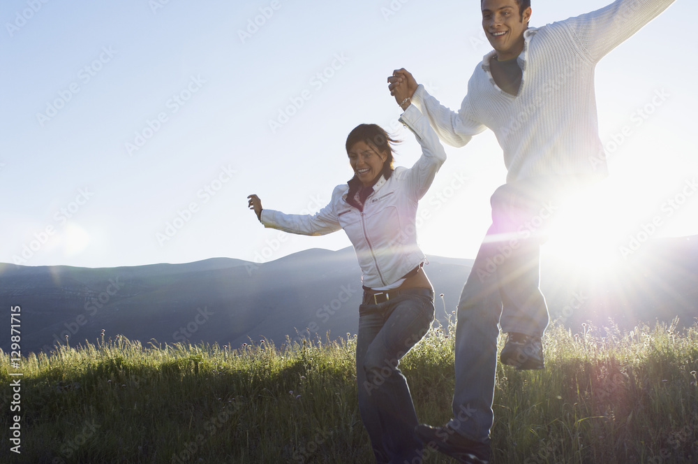 Happy young multiethnic couple jumping while holding hands in park - obrazy, fototapety, plakaty 