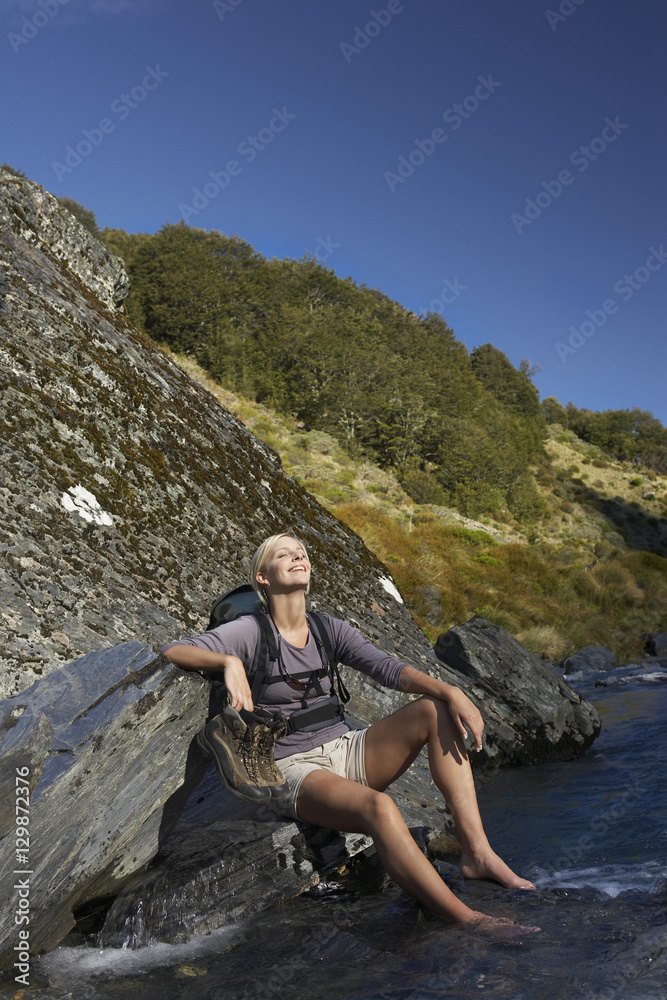Relaxed young woman dipping her feet in forest river