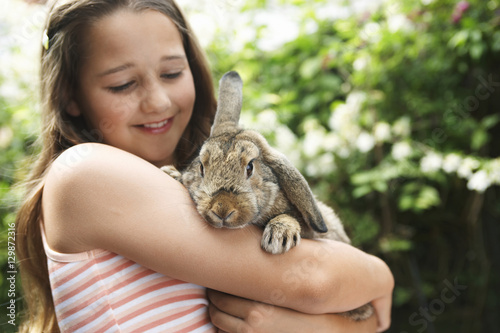 Happy young girl holding bunny rabbit in the backyard