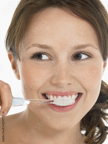 Closeup of a young woman brushing teeth against white background