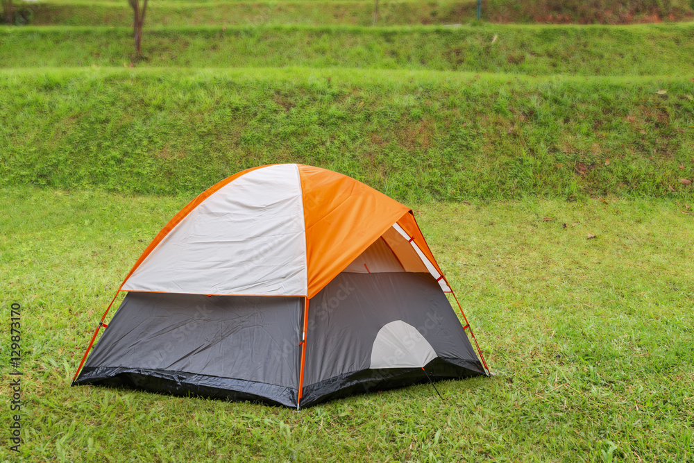 Orange dome tent on green grass in camping site