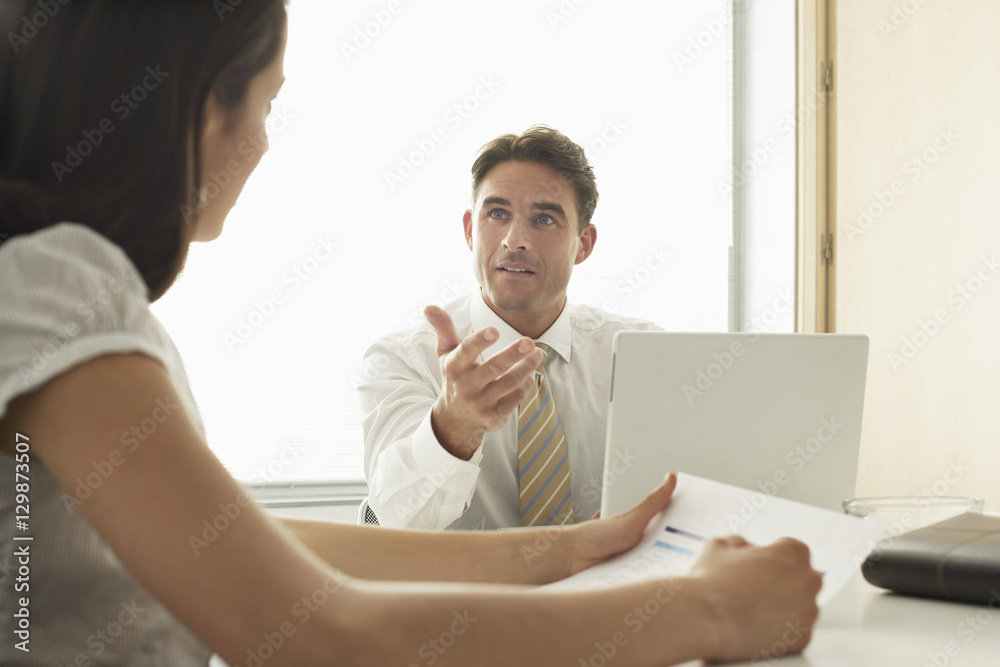 Young businessman discussing with female colleague at desk in office