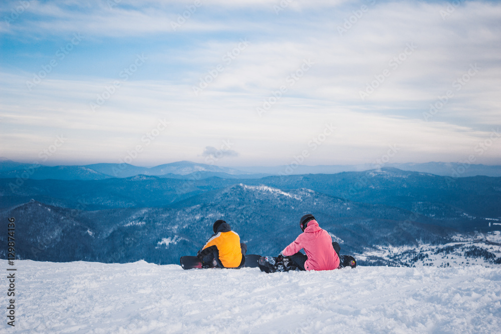 Two sportsmen snowboarders sit and prepare for descent from snow