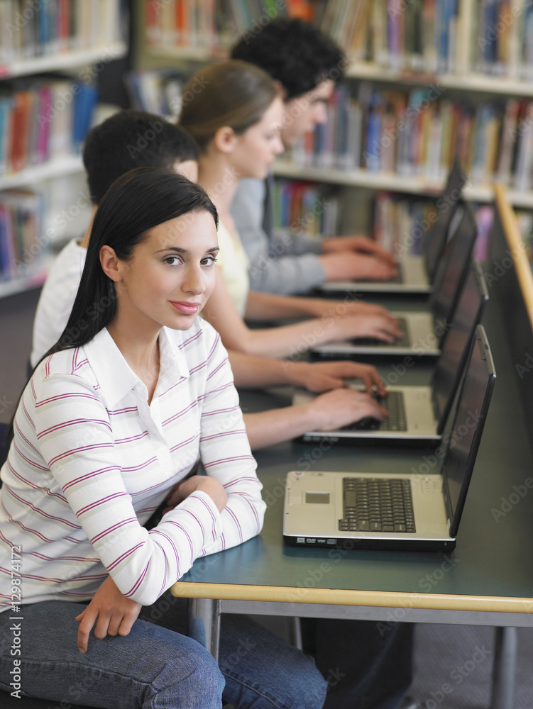 Portrait of teenage girl with friends in row using laptops in library Portrait of teenage girl with friends in row using laptops in library