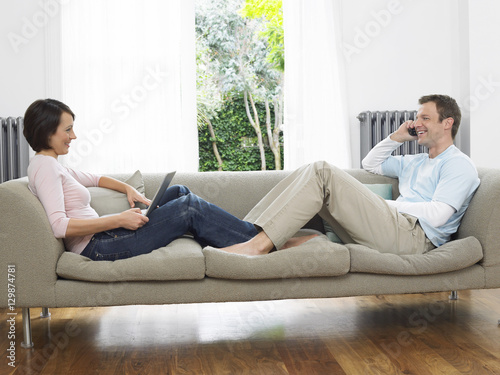 Side view of a relaxed couple using laptop and cellphone on couch