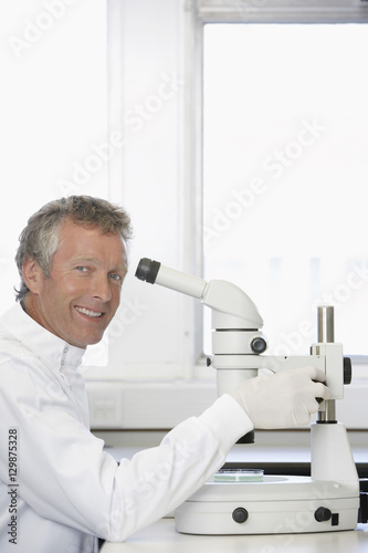 Portrait of happy middle aged scientist using microscope in laboratory