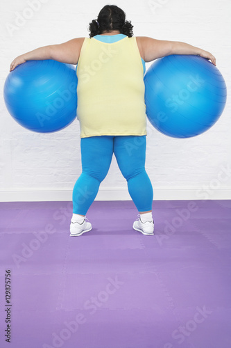 Rear view of an overweight woman holding two exercise balls in healthclub