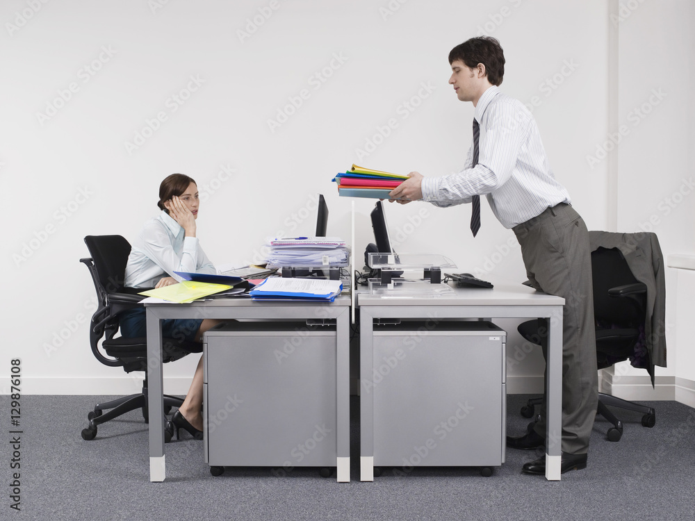 Side view of a businessman passing folders to female colleague across the desk Side view of a businessman passing folders to female colleague across the desk