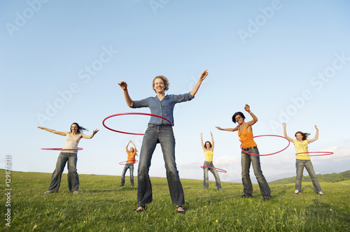 Full length of happy female friends playing with hula hoop against sky in park