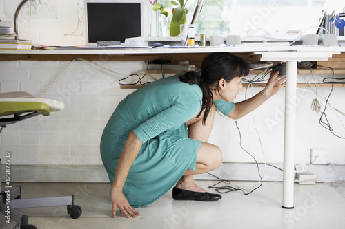 Canvas Print Side view of young businesswoman adjusting cables under desk