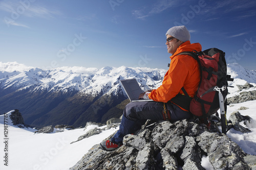 Side view of a male mountain climber using laptop on mountain peak