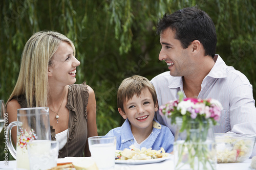 Happy young boy with parents looking at each other while sitting at dining table in garden
