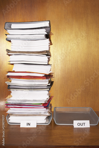 Inbox with stack of paperwork empty outbox on desk
