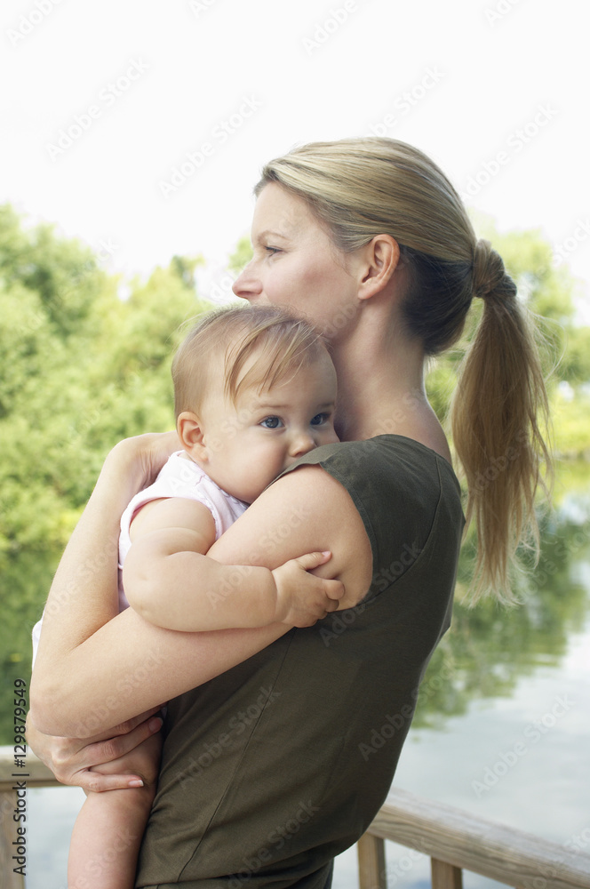 Side view of a young mother carrying daughter against the lake Side view of a young mother carrying daughter against the lake