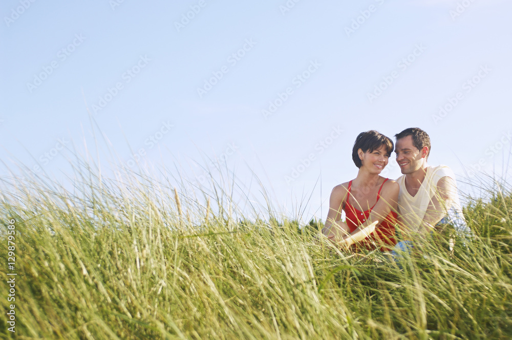 Young romantic couple sitting in tall grass at beach Young romantic couple sitting in tall grass at beach