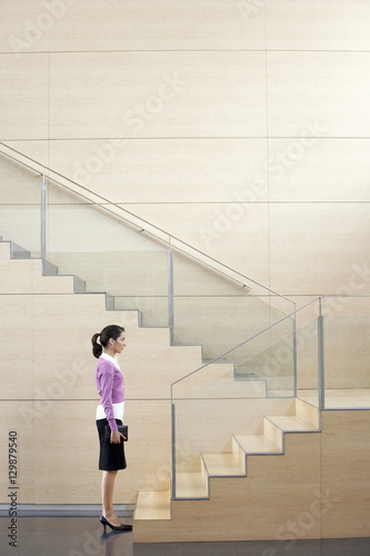 Profile shot of young businesswoman with diary standing in front of steps in office