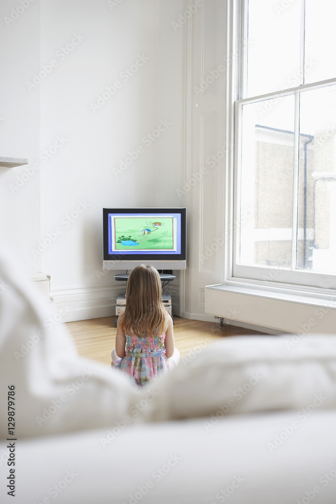 Obraz premium Rear view of a little young girl watching cartoons in television at home